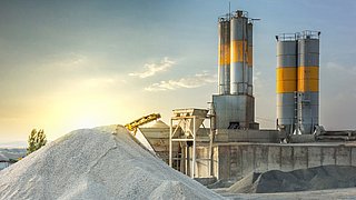 Foto, Blick auf eine Zementwerk unter blauem Himmel. Im Vordergrund ein großer Sandberg