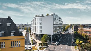 Foto, modernes, mehrstöckiges Haus an der Ecke zweier spitz aufeinander zulaufender Straßen.