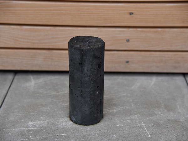 Foto, ein dunkelgrauer Testzylinder aus Klimabeton
