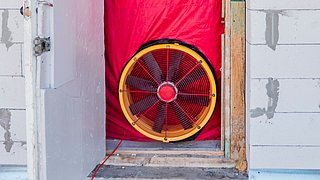 Foto, Tür eines im Bau befindlichen Hauses mit einem eingesetzter Ventilator zur Durchführung eines Blower-Door-Tests.