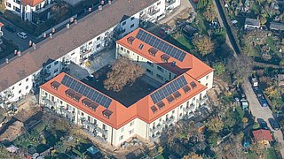 Foto, Aufnahme aus der Luft auf U-förmiges Mehrfamilienhaus mit Photovoltaik-Kollektoren auf dem Dach.