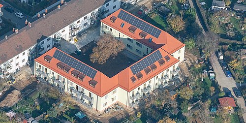 Foto, Aufnahme aus der Luft auf U-förmiges Mehrfamilienhaus mit Photovoltaik-Kollektoren auf dem Dach.