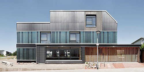 Foto, Frontalansicht auf modernes Einfamilienhaus mit dunkler Fassade, verschiedenen Fassadenelementen und asymmetrischer Form. 
