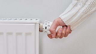 Foto einer Hand, die an einem Heizungsthermostat dreht