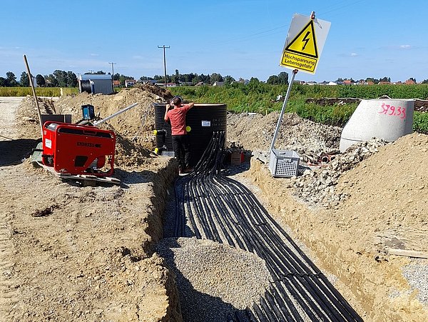 Foto, mehrere Leitungen liegen in einem Sammelschacht auf einer Baustelle