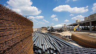 Foto, gelagerte Baustoffe und -materialien auf einer Baustelle, im Hintergrund ein Betonmischer.