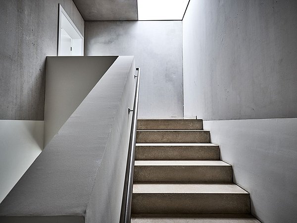 Foto, Treppenaufgang mit Betonstufen und schlichtem Handlauf in einem modernen, minimalistisch gestalteten Innenraum