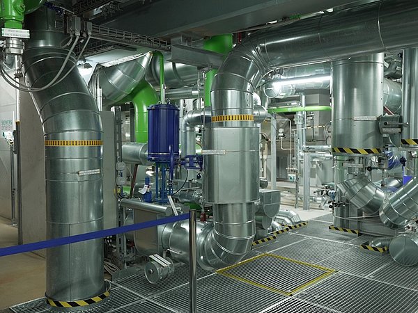 Foto, Innenansicht einer Hochtemperatur-Wärmepumpe mit großen silbernen Rohren und grünen Ventilen in einer technischen Anlage.