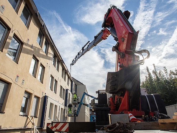 Foto, Hausfassade an der Fassadenelemente angebracht werden. Rechts steht ein Baufahrzeug.