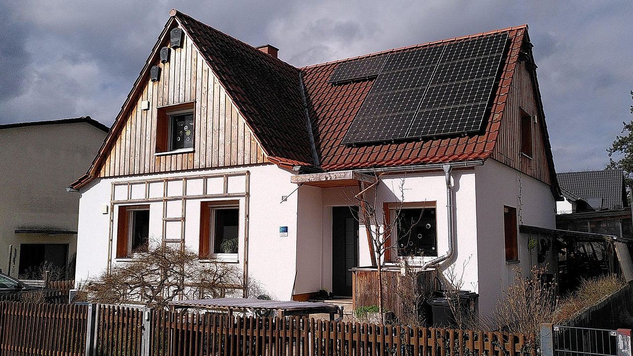 Foto, Einfamilienhaus mit teilweiser Holzverkleidung an der Fassade und Photovoltaikanlage auf dem Dach. 