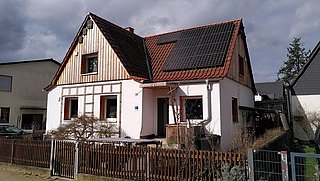 Foto, Einfamilienhaus mit teilweiser Holzverkleidung an der Fassade und Photovoltaikanlage auf dem Dach. 