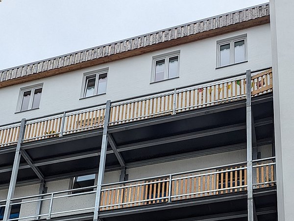 Foto, Mehrstöckiges Wohngebäude mit mehreren Balkonen, die teilweise mit Holzverkleidung und Metallgeländern ausgestattet sind