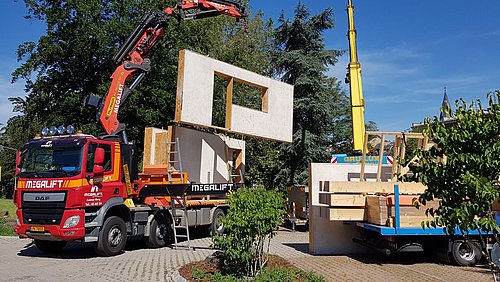 Foto, ein LKW hebt auf einer Baustelle mittels Kran vorgefertigte Fassadenelemente in die Höhe.