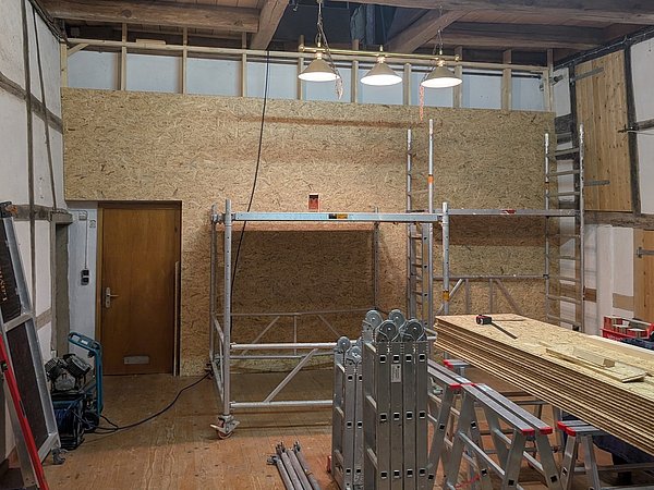 Foto, Innenraum einer Werkstatt mit Holzplatten, Gerüst, Werkzeugen und einer Holztür