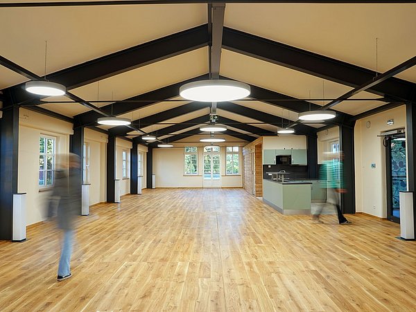 Foto, Großer, stützenfreier Dachraum mit Holzboden, sichtbaren Stahlträgern und moderner Küchenzeile am Ende