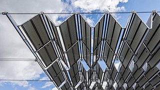 Foto, Blick von unten auf ein Solarfaltdach vor einem Hintergrund aus blauem Himmel und weißen Wolken.