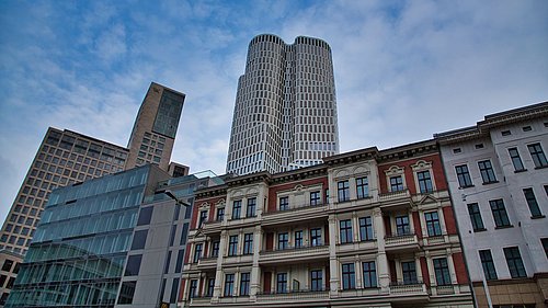 Foto, Hochhäuser und Altbauten unter blauem Himmel mit leichten Wolken.