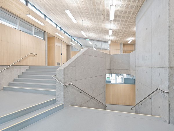 Foto, Treppenhaus mit Treppen und Wänden aus Beton. Die Decke und Teile der Wände sind mit Holz verkleidet.