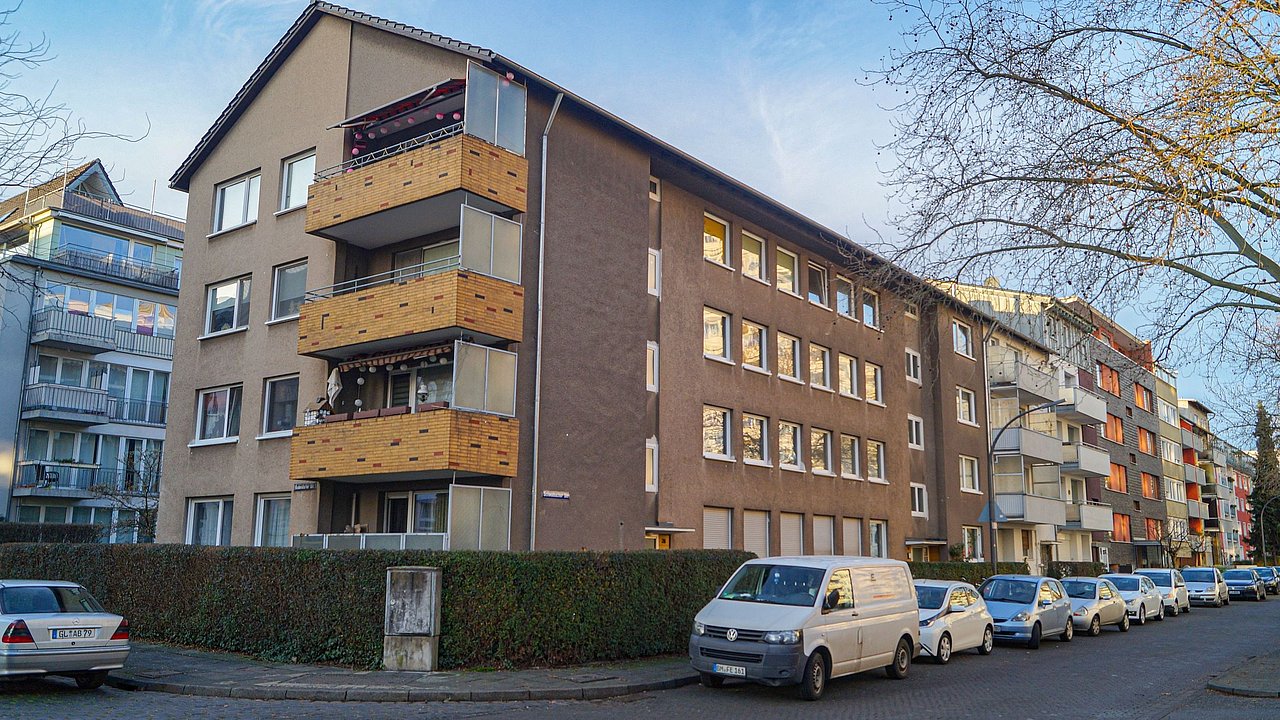 Foto, Mehrstöckiges Wohngebäude mit Balkonen an der Straßenseite, mehrere geparkte Autos entlang der Straße