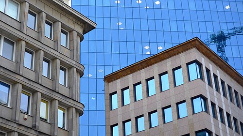 Foto, mehrere mehrgeschossige Gebäude, im Hintergrund ein großes Hochhaus mit Glasfassade.