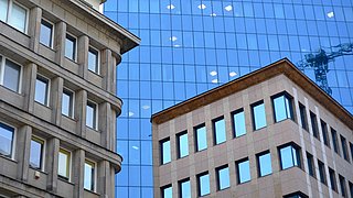 Foto, mehrere mehrgeschossige Gebäude, im Hintergrund ein großes Hochhaus mit Glasfassade.