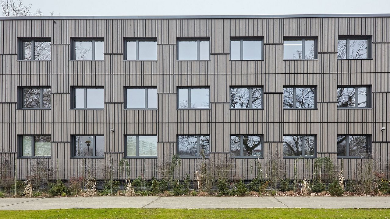 Foto, erneuerte Fassade vom Verwaltungsgebäude mit grauer Holzverkleidung.