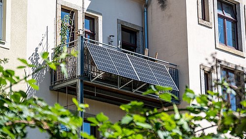 Foto, Balkon mit montierten Solarpaneelen an einem mehrstöckigen Wohnhaus mit Fenstern.