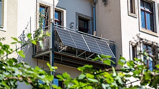 Foto, Balkon mit montierten Solarpaneelen an einem mehrstöckigen Wohnhaus mit Fenstern.