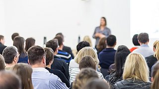 Foto, eine Gruppe von MEnschen verfolgt einen Vortrag