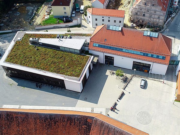 Foto, Luftaufnahme eines Gebäudes mit begrüntem Flachdach und umliegenden Gebäuden