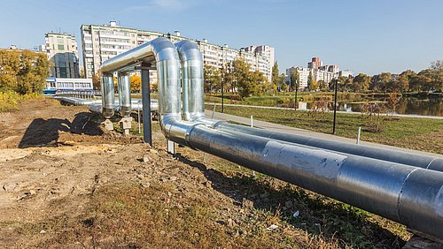 Foto, neu gebaute Fernwärmerohre führen zu einem mehrstöckigen Gebäude im Hintergrund.