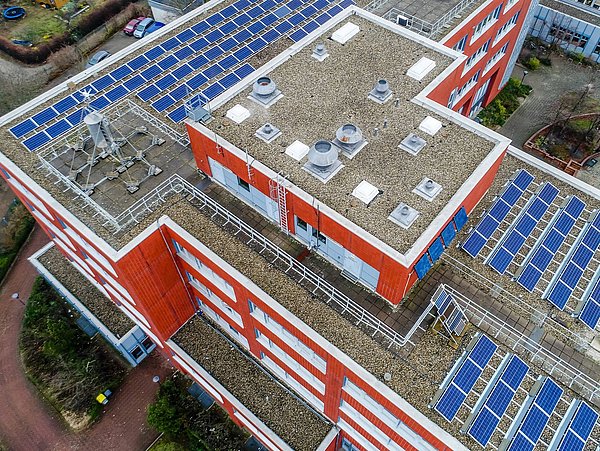 Foto, Luftbild eines mehrstöckigen Gebäudes mit einer PV-Anlage auf dem Dach.