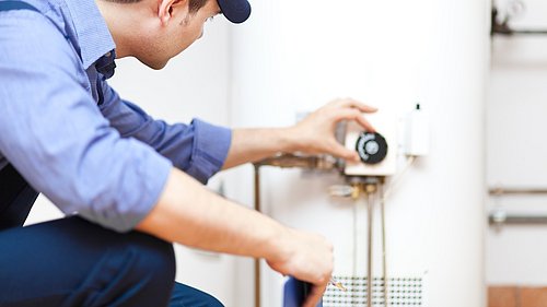 Foto, Techniker in blauer Uniform und Kappe bedient eine Heizungsanlage.