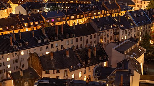 Foto, Dachlandschaft eines Wohnviertels mit beleuchteten Fenstern in der Abenddämmerung.