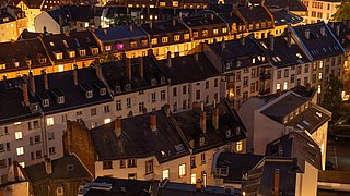 Foto, Dachlandschaft eines Wohnviertels mit beleuchteten Fenstern in der Abenddämmerung.