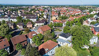 Foto, Luftaufnahme einer deutschen Kleinstadt mit roten Ziegeldächern, einer Kirche mit Turm und vielen Bäumen
