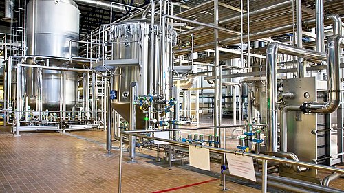 Foto, Innenansicht einer Industriehalle mit vielen Leitungen und mehreren Tanks aus Edelstahl.
