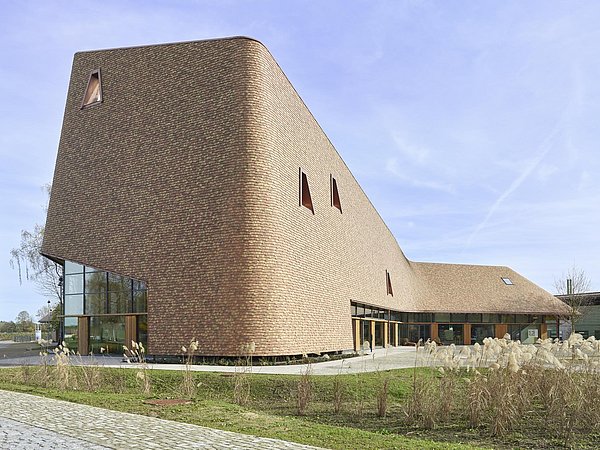 Foto, Gebäude eines Besucherzentrums mit geschwungener Fassade aus braunen Ziegeln und großen Fenstern