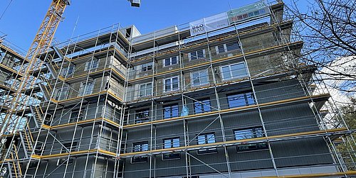 Foto, Mehrstöckiges Wohngebäude in Gerüstbauphase mit Baukran und blauem Himmel im Hintergrund