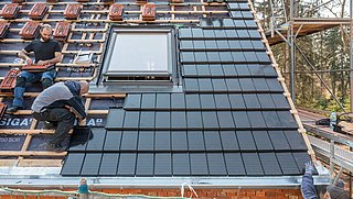 Foto, mehrere Personen montieren Photovoltaik-Dachziegel auf einer Baustelle..
