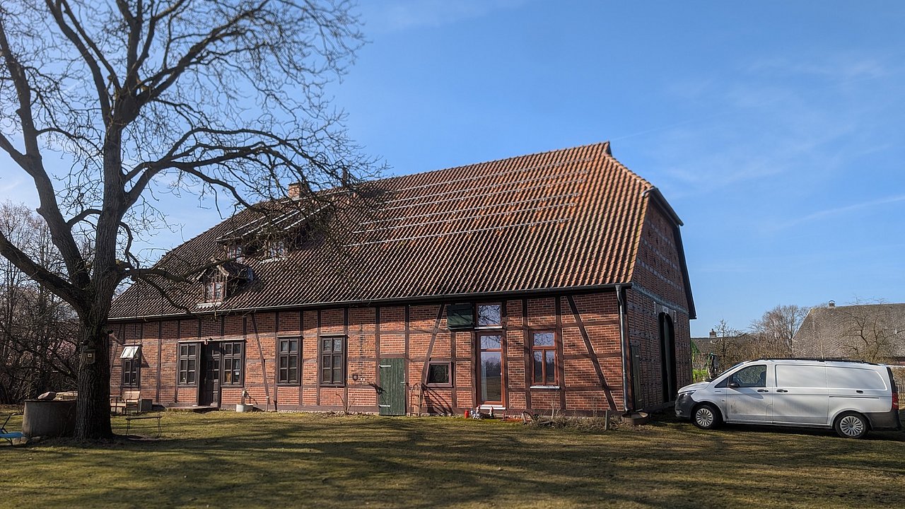 Foto, Backsteingebäude mit Satteldach, davor ein Baum und ein weißer Transporter auf einer Rasenfläche