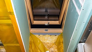 Foto, Fenster mit Holzrahmen in einer Wand mit grüner Gipskartonplatte und gelber Dämmung auf dem Boden.