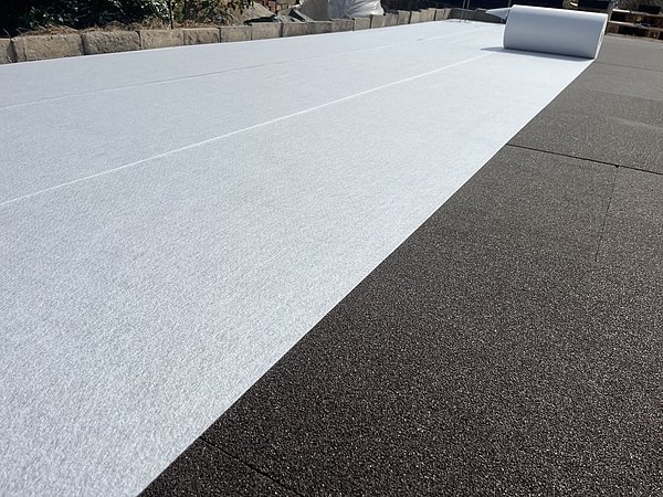 Foto, eine Bahn aus weißem Flies ausgerollt auf schwarzen Fundamentplatten.