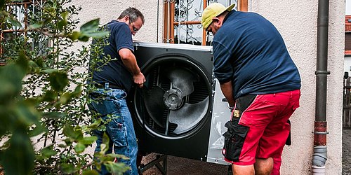 Foto, zwei Männer tragen die Außenanlage einer Wärempumpe