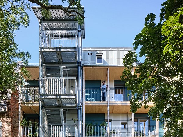 Foto, Mehrstöckiges Wohngebäude mit Außentreppe und Balkonen, umgeben von Bäumen