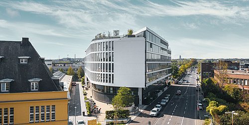 Foto, modernes, mehrstöckiges Haus an der Ecke zweier spitz aufeinander zulaufender Straßen.