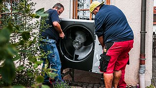 Foto, zwei Männer tragen die Außenanlage einer Wärempumpe