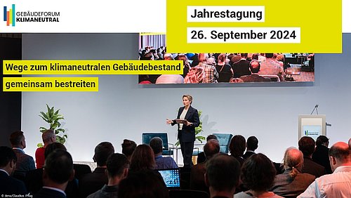 Foto, Menschen sitzen vor einer Bühne, auf der ein Vortrag gehalten wird, dazu der Text "Jahrestagung 26. September 2024; Wege zum klimaneutralen Gebäudebestand gemeinsam bestreiten".