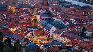 Foto, Abendliche Luftaufnahme einer Altstadt mit einer großen Kirche im Zentrum und beleuchteten Straßen.