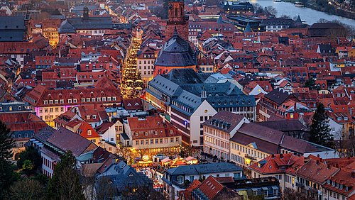 Foto, Abendliche Luftaufnahme einer Altstadt mit einer großen Kirche im Zentrum und beleuchteten Straßen.
